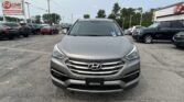 Front view of a gray Hyundai SUV parked in a car dealership lot with other vehicles and an EZ LOAN Auto Sales sign in the background.