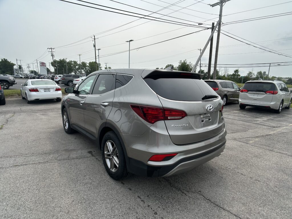 Silver Hyundai Santa Fe SUV in a crowded dealership parking lot with power lines overhead and a Toyota sign in the distance.