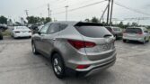 Silver Hyundai Santa Fe SUV in a crowded dealership parking lot with power lines overhead and a Toyota sign in the distance.