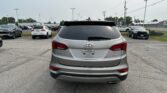 Rear view of a silver Hyundai Santa Fe Sport in a parking lot, with other cars and power lines in the background.