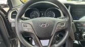 Close-up of a car steering wheel and instrument cluster from the driver's seat, with a parking lot visible through the windshield.