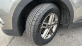 Close-up of a car wheel and tire, showing treads and alloy rim with gray bodywork and wheel well mud.