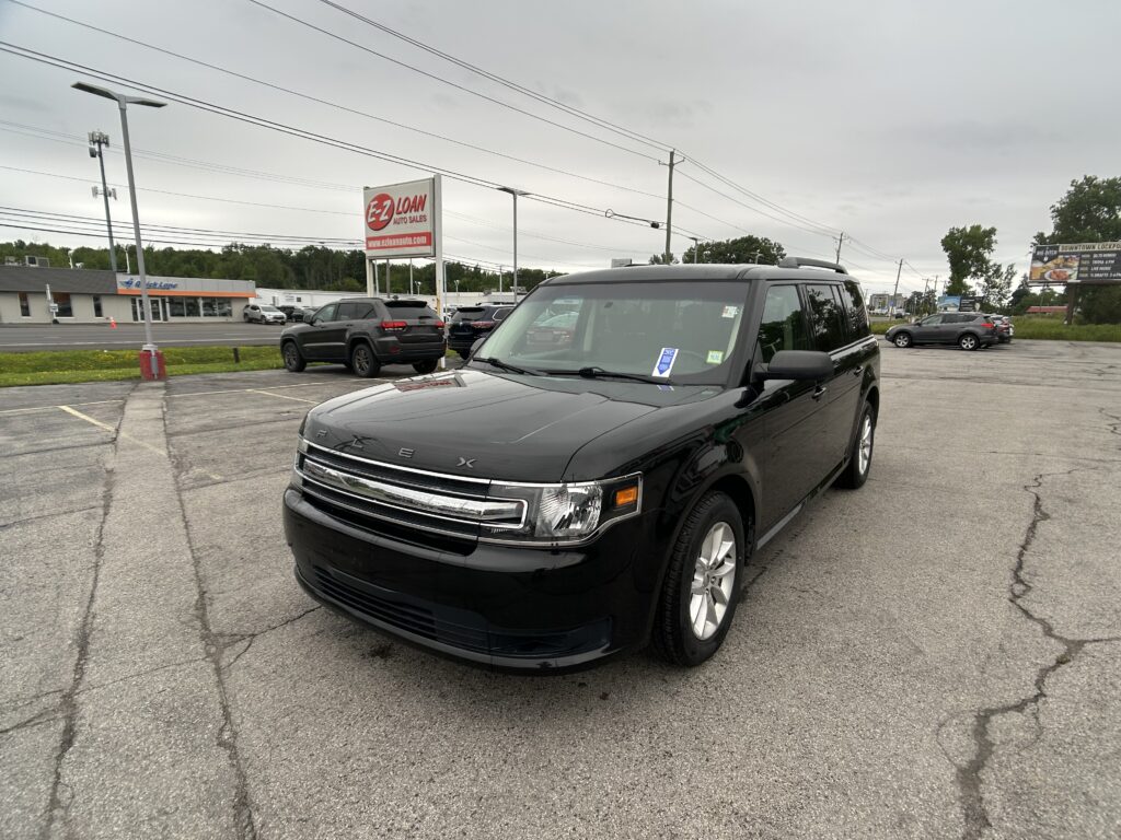 Black SUV in a dealership parking lot with an EZ LOAN Auto Sales sign in the background on an overcast day.