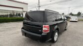 Rear view of a glossy black SUV with visible tail lights and roof rails in a dealership parking lot under an overcast sky.