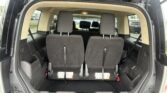Open-rear-view of SUV interior showing two upright third-row seats with headrests, cargo area clear, parked cars visible outside, and seat‑back labels on the floor.