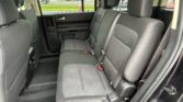Interior of a dark fabric SUV back seat with three seats, headrests, and visible seatbelts; street scene seen through the windows.