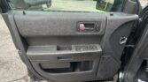 Driver-side car door interior with chrome handle and window controls; visible parking lot with cars outside the window.