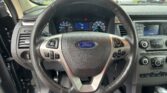 Close-up of a Ford steering wheel from the driver's seat, with the instrument cluster and center console visible in a parking lot exterior view.