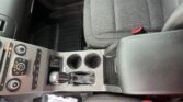 Center console of a car with gear shifter, two cupholders, climate controls, and a front seat with a red seatbelt buckle visible on the right.