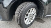 Close-up of a car tire and alloy wheel in the front wheel well with a black fender and dirt specks.