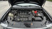 Car hood raised to reveal the engine bay with battery, fluid reservoirs, and hoses visible in a parking lot scene from above