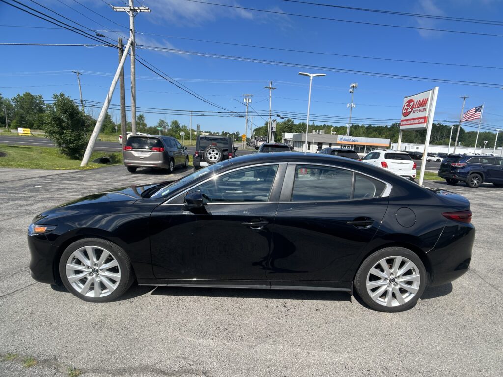 Close-up of a shiny black sedan in a car dealership lot with other vehicles and a large ELoan Auto Sales sign in the background under a clear blue sky