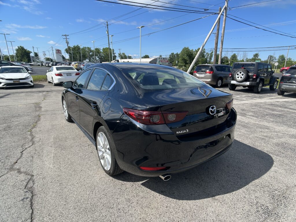 Black Mazda3 in the foreground at a car dealership lot with other cars and a blue sky above it.