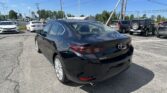 Black Mazda3 in the foreground at a car dealership lot with other cars and a blue sky above it.