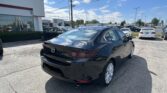 Black Mazda sedan visible in the dealership lot with a Toyota showroom in the background on a sunny day.