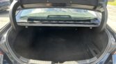 Open trunk of a dark sedan, revealing a large empty cargo area with black carpeting and the rear window.