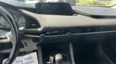Driver’s-seat view of the dashboard, gear selector, and center screen, with a busy parking lot outside.