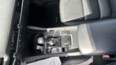 Front interior of a car showing the center console with gear shifter, control knob, and black leather seats.
