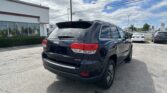 Rear three-quarter view of a black Jeep SUV (Limited) parked in a dealership lot, with a white building and Toyota signs in the background.