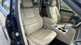 Beige leather SUV interior with front and back seats, view from open driver's door, center console visible