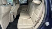 Interior of a beige leather SUV with rear row seats visible, door open showing a dark floor mat and seat belts ready for passengers
