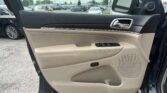 Interior car door panel with beige upholstery, window control buttons, and speaker, view of parking lot through open door window and side mirror