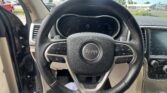 Steering wheel and dashboard in a Jeep, speedometer at 0 and an open driver's door visible to the left, parking lot outside.