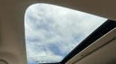Open panoramic sunroof in a car, showing a blue sky with light clouds from inside the vehicle.