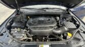 Under-hood view of a vehicle with the hood up, showing a V6 engine cover at the center and various hoses and components around it.