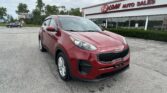 Red Kia SUV parked in the foreground outside a white building with 'EZ LOAN AUTO SALES' sign in red letters.