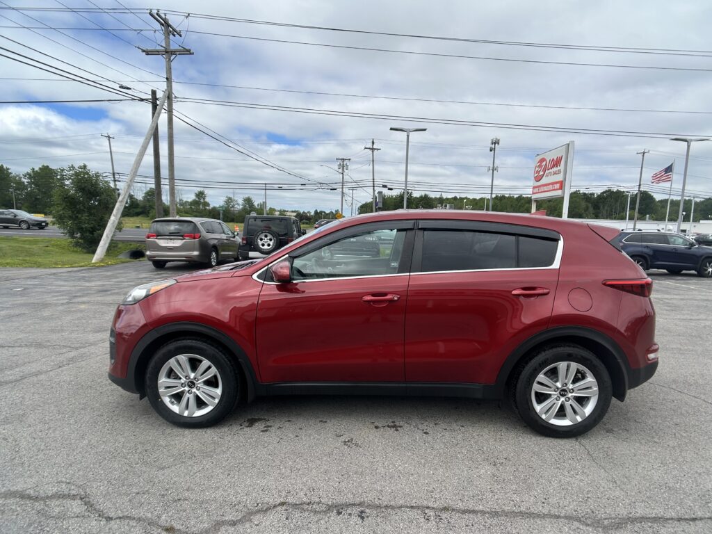 Red SUV in a dealership lot with power lines overhead and an American flag in the background.