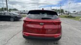 Rear view of a red Kia Sportage SUV in a parking lot with other cars and overhead power lines in a cloudy day setting.