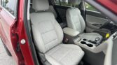 Interior of a red sedan showing front seats with light gray fabric upholstery and center console viewed from the open door.
