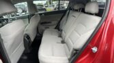Rear row of gray fabric seats in a red SUV, three headrests, safety belts visible, door open to outside showroom.