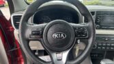 View of a car interior from the driver's seat, focusing on the Kia steering wheel with control buttons and the dashboard ahead.
