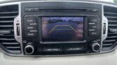 In-dash display showing rear-view camera with parking guidelines over a parking lot scene, surrounded by car controls and vents