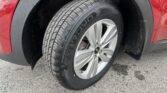 Close-up of a red car's front wheel with a treaded tire and alloy rim, a wet fender in view.