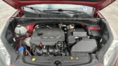 Red car with hood raised, exposing the engine bay and front grille area, view of coolant reservoir and wiring.