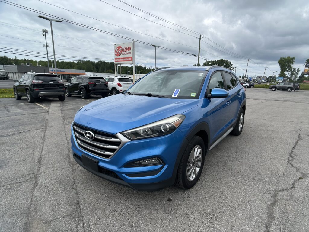 Blue Hyundai SUV parked in a car lot with other vehicles and a large EZ Loan Auto Sales sign in the background under a cloudy sky