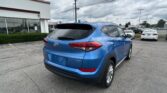 Blue Hyundai SUV parked in a dealership lot, rear-three-quarter view with a white building on the left and overcast sky above.