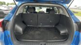 Open hatchback of a blue SUV showing the spacious cargo area with rear seats upright and a black rubber mat in the trunk.
