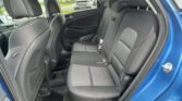 Back seat of a blue car with black fabric upholstery and three visible seat belts and headrests on the bench.
