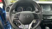 Driver's perspective of a car interior: steering wheel, instrument cluster, center touchscreen, and parking lot through the windshield.