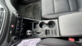 Inside a car’s front cabin showing the center console with the gear shifter, cup holders, and climate controls near the dash edge and seat.
