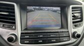 Car dashboard screen showing rear-view camera view with yellow and red distance lines and safety text.