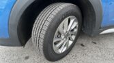 Close-up of a car tire on a silver alloy wheel mounted to a blue vehicle, with the wheel well visible in the background.