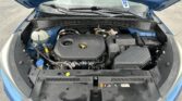 Open car hood showing engine bay with various hoses, reservoir, and battery in a blue vehicle