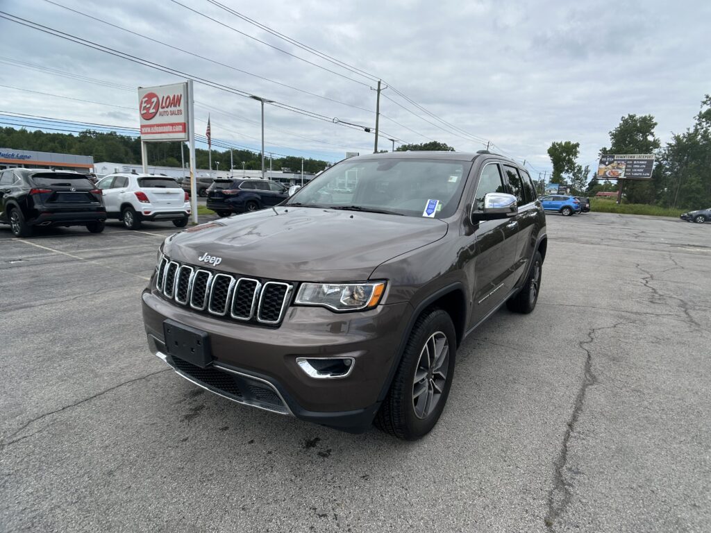Gray Jeep SUV in a crowded car dealership lot under a cloudy sky, with a large EZ Loan Auto Sales sign nearby.