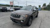 Gray Jeep SUV in a crowded car dealership lot under a cloudy sky, with a large EZ Loan Auto Sales sign nearby.