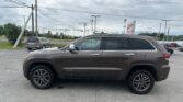 Brown Jeep Grand Cherokee in a dealership parking lot with power lines overhead and a cloudy sky behind it.
